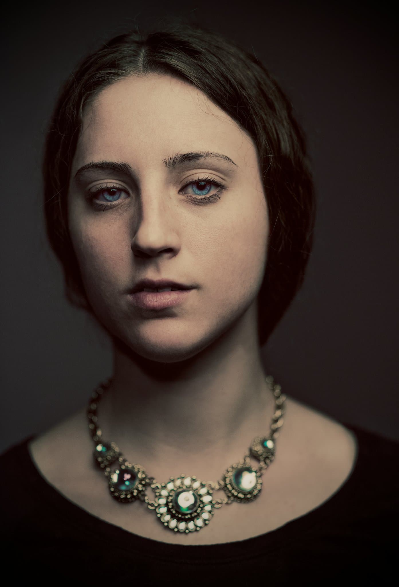 A dim, moody studio portrait with vintage lighting and minimal styling.
