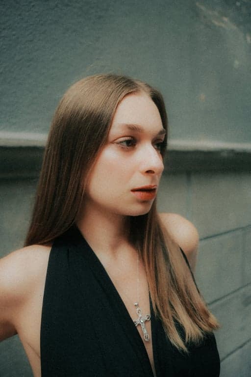 Extend the original image of the person into a complete full-body view while preserving the same individual, facial identity, clothing, and studio environment. Reconstruct the missing lower body with natural human proportions, relaxed upright posture, balanced anatomy, and lighting that matches the original image so the result appears as a single uninterrupted full-body photo.