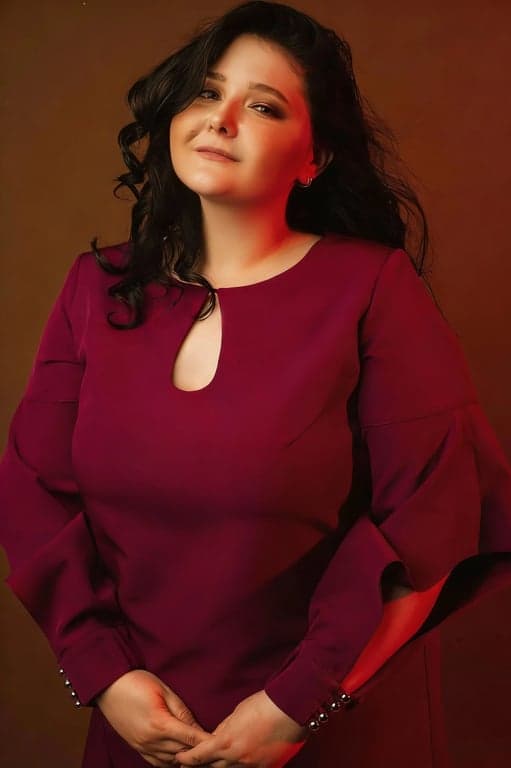 a portrait of a person photographed at eye level in a head-and-shoulders crop, front-facing or slight three-quarter angle; strongly reduce the appearance of a double chin by visibly compressing and tightening the under-chin area, clearly reshaping the jaw-to-neck separation so the chin appears slimmer and more lifted; preserve original facial identity and bone structure; maintain natural skin texture and pores; avoid plastic blur or warping; do not modify or replace the background; the slimming effect must be clearly noticeable at first glance