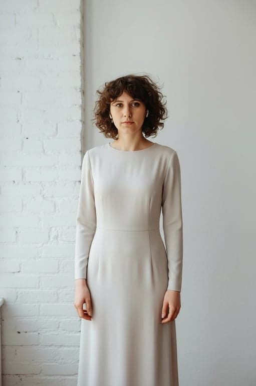 a portrait of a person dressed in a minimalist long-sleeve dress with precise cut, subtle seam lines, fluid fabric movement, calm posture, soft neutral illumination