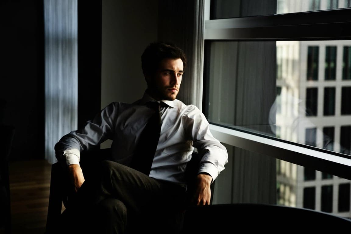 A high contrast portrait of a man, intense shadow detail, glowing highlights on skin and hair, sharp clarity, urban background with hard lines.