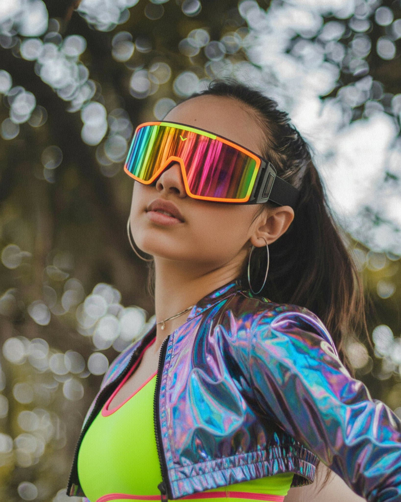Vibrant holo jacket and neon sportswear paired with oversized rainbow visor in sunlit woods.
