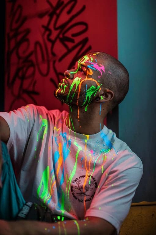 a portrait of a person with neon paint splashes or drips glowing brightly on their skin and clothes under black light
