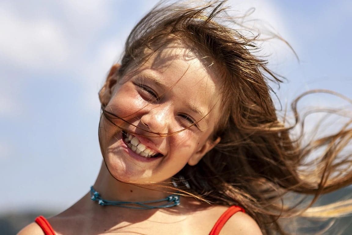 AI teeth whitening filter before photo - girl with windblown hair laughing near sky